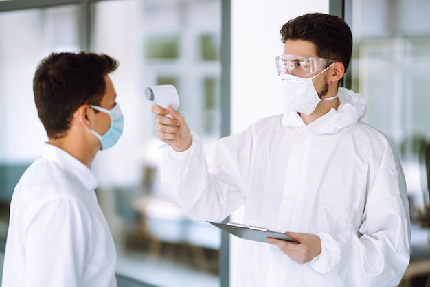 Disease control expert with an Infrared thermometer equipment to check the temperature at office