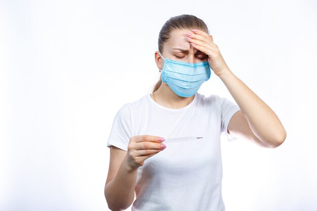 Больная женщина в защитной медицинской хирургической маске с термометром в руке лечится от вируса. Изолированные на белом фоне