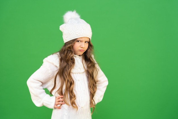 孤立した背景に帽子とセーターを着た不機嫌な少女子供は外の寒さに動揺しています