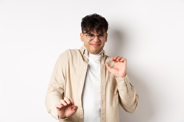 Disgusted guy grimacing and jumping away from something nasty, stare with aversion and dislike, rejecting bad offer, standing on white wall.