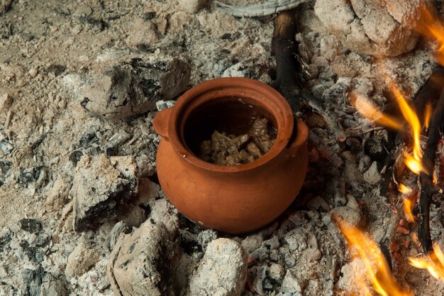 A dish in a clay pot is prepared on burning coals. the dish is cooked and smoked on charcoal