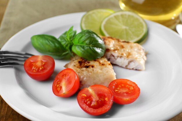 Блюдо из рыбного филе с базиликом и помидорами на тарелке крупным планом