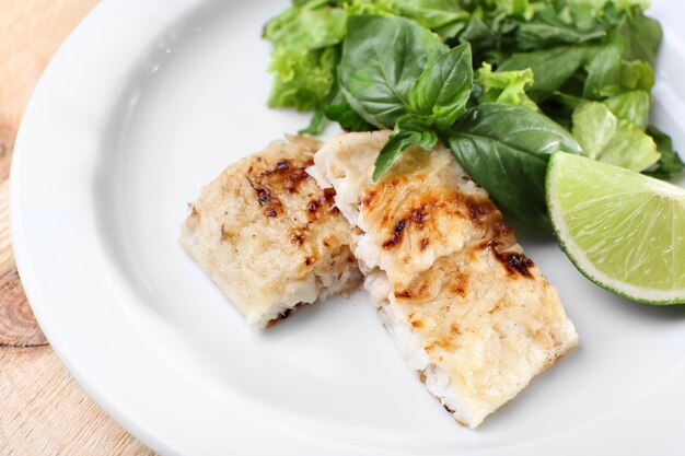 Photo dish of fish fillet with greens and lime on plate close up