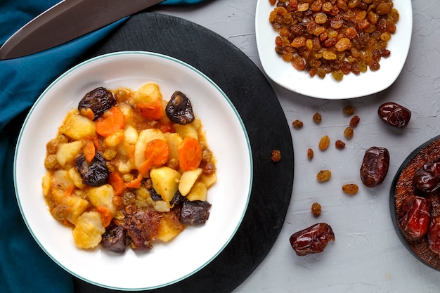 A dish of jewish cuisine sweet tsimes with carrots vegetarian dates in a plate on a round stand on a concrete surface near dates raisins