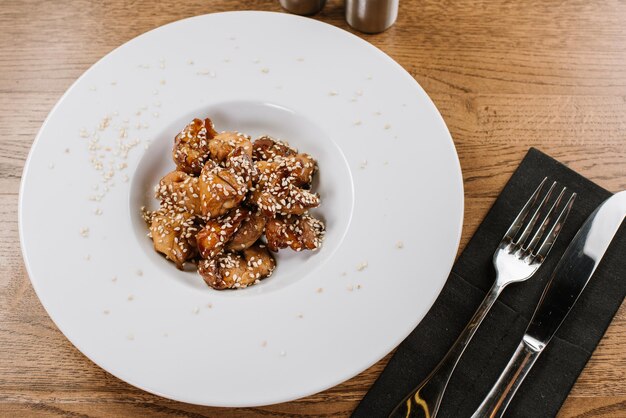 Dish of roasted meat with sesame and sauce on wooden background