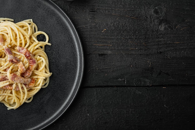 Dish of Spaghetti Carbonara, modern italian recipe of pasta with guanciale, egg ad pecorino romano cheese set, on black wooden table, top view flat lay, with copy space