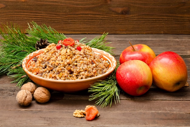 Dish of traditional Slavic treat on Christmas Eve on brown wooden table. Pine branches, apples, walnuts.