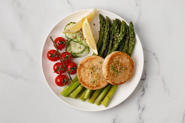 Dish with cutlets with vegetables asparagus cucumbers and tomatoes cherry on white plate