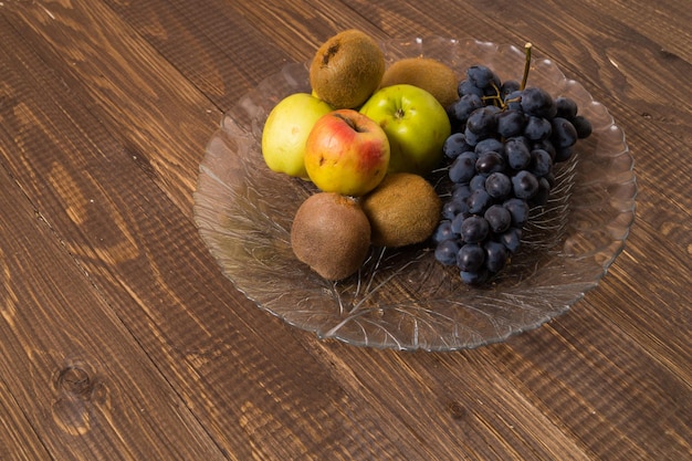 A dish with different fruit is on the table. Among them are apples, kiwi and grapes