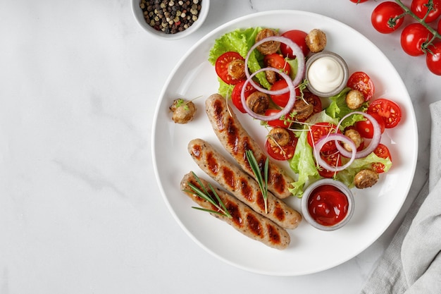 Dish with Grilled sausages and vegetable salad with lettuce and tomatoes on white plate