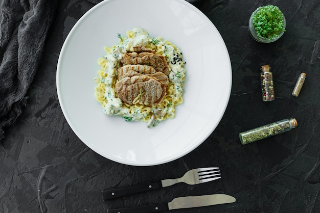 Piatto con pezzi di carne, pasta, verdure, salsa di foie gras e terra verde oliva