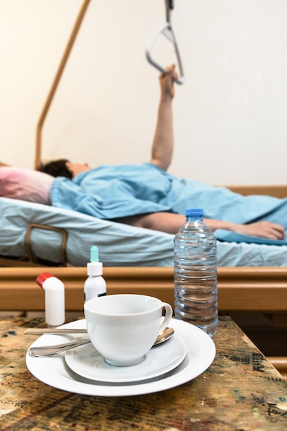 Dishes on table and patient holding handle on bed