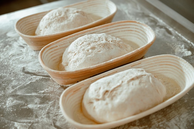 Dishes with raw bread loafs on table with scattered flour in modern bakery