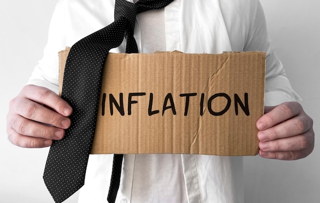 A disheveled business man holds up a cardboard sign with the words Inflation