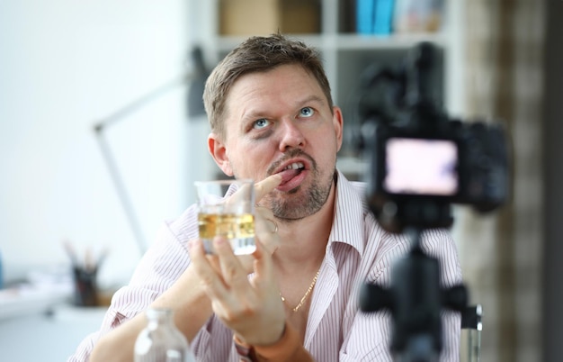 Disheveled man hold glass of alcohol in his hand and taste it with his finger