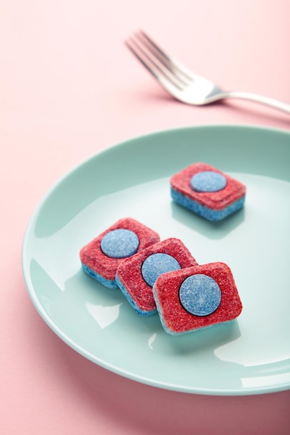 Dishwasher detergent tablet with fork and dishes on pink background Vertical photo