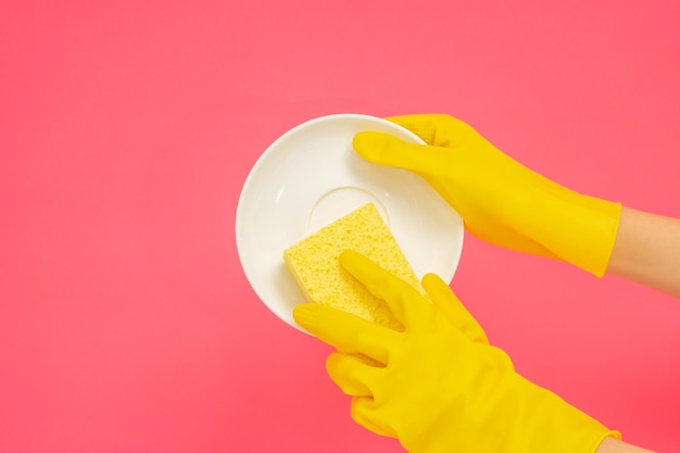 Dishwashing concept hands in rubber gloves to holding yellow\
sponge and wash the dishes