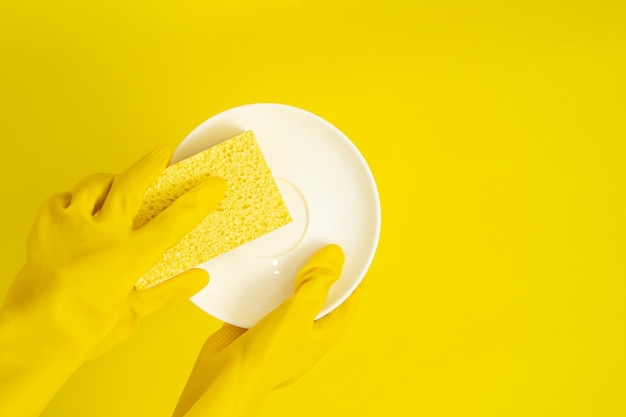 Dishwashing concept hands in rubber gloves to holding yellow\
sponge and wash the dishes