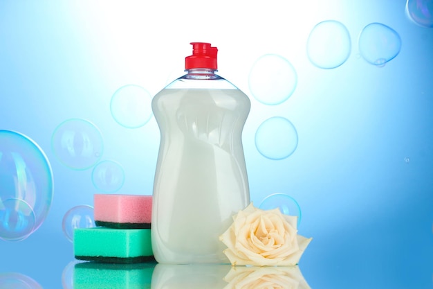 Dishwashing liquid with sponges and flower on blue background