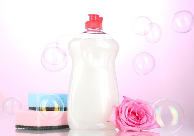 Dishwashing liquid with sponges and flower on pink background