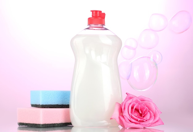 Dishwashing liquid with sponges and flower on pink background