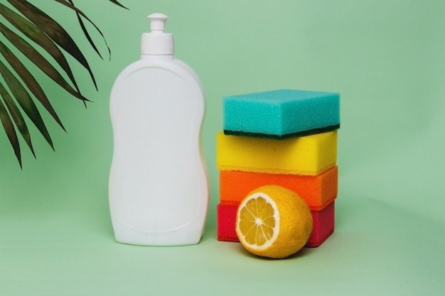 Dishwashing liquid with sponges and lemon on green background