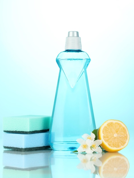 Dishwashing liquid with sponges and lemon with flowers on blue background