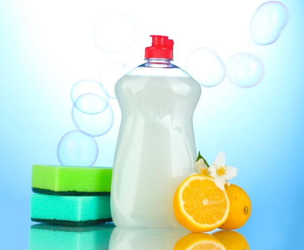 dishwashing liquid with sponges and lemon with flowers on blue background