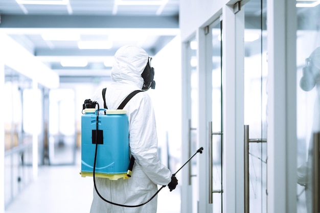 Disinfecting of office to prevent COVID-19, Man in protective hazmat suit with with spray chemicals.