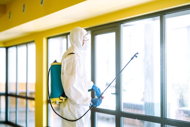 Disinfecting of office to prevent COVID19 Man in protective hazmat suit Cleaning concept