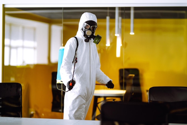 Disinfecting of office to prevent COVID19 Man in protective hazmat suit with with spray chemicals