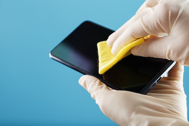 Фото Дезинфекция смартфона желтой салфеткой с антибактериальной пропиткой в ручных перчатках