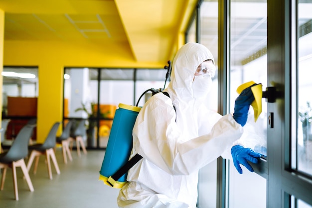 Un disinfettante in tuta protettiva e maschera lava l'ufficio