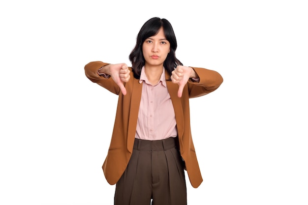 嫌い嫌いなアジア人女性が親指を下に向けて顔をゆがめ、白い背景の上に立っていると不平を言っている。