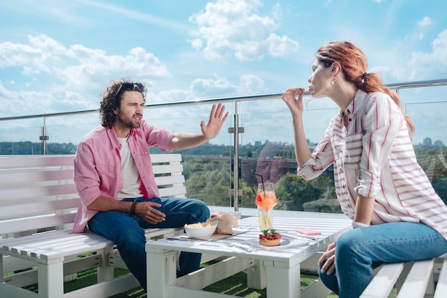 Photo dislike of manners. curly handsome man not liking manners of his girlfriend while having romantic dinner