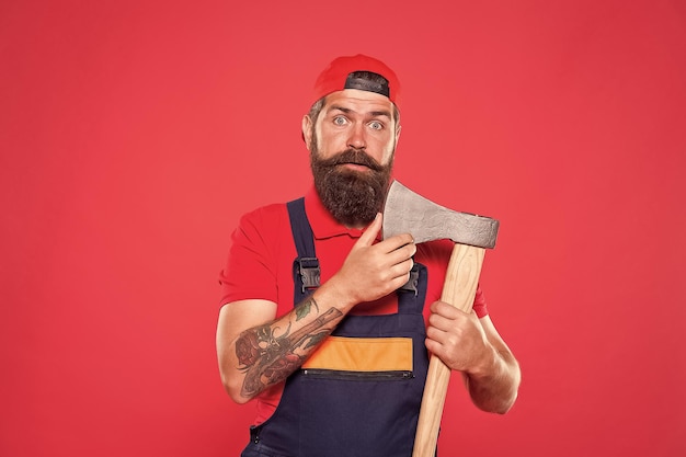 Dismantling and demolition of structures Bearded lumberjack Man builder uniform hold axe Man builder hold ax red background Renovation concept Bearded handyman Brave worker Brutal job