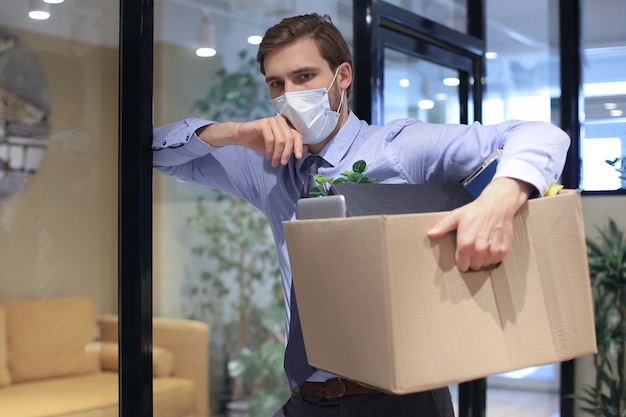 Photo dismissal employee in preventive medical mask in an epidemic coronavirus. dismissed worker going from the office with his office supplies.