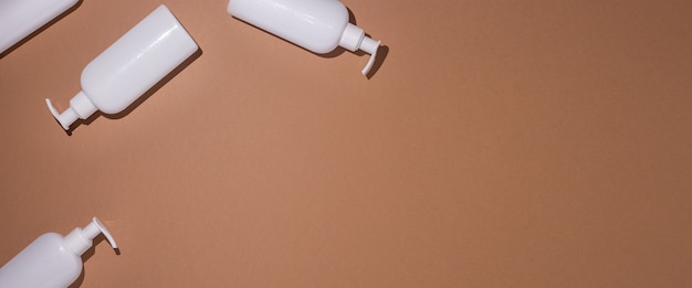 Dispenser bottles lie on a brown cardboard background. Top view, flat lay. Banner.