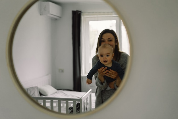 Displaying in the mirror how a mother plays with her child. Mother of a nursing baby. Happy motherhood. The family is at home. Portrait of a happy mother and child.