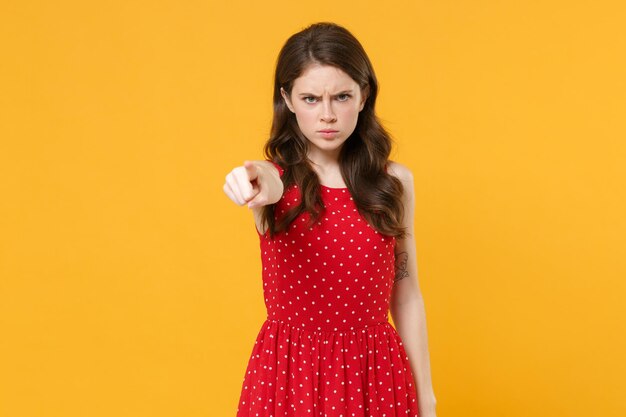 Displeased angry young brunette woman girl in red summer dress posing isolated on yellow wall backgr