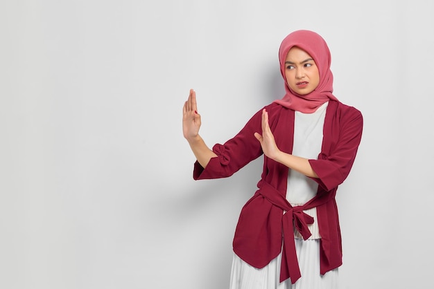 Displeased beautiful asian woman in casual shirt showing stop
gesture saying no expressing rejection isolated over white
background