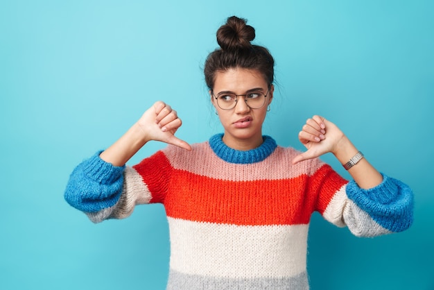 displeased beautiful woman in eyeglasses showing her thumbs down isolated over blue wall