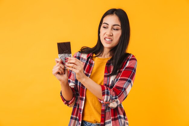 displeased caucasian woman expression disgust and holding chocolate isolated over yellow wall