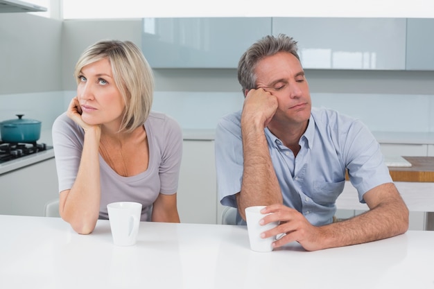 Photo displeased couple sitting with coffee cups in kitchen