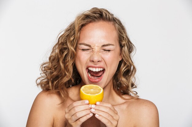 사진 반쯤 벗은 여자가 찡그린 채 흰 벽에 격리된 레몬을 먹고 있다