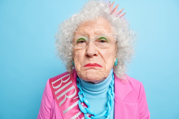 Displeased lonely retired old woman has wrinkled well cared face looks disappointed and gloomy celebrates birthday alone dressed in stylish clothes