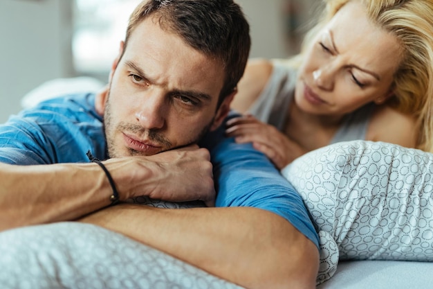 Displeased man ignoring his girlfriend while lying down in bed after the argument