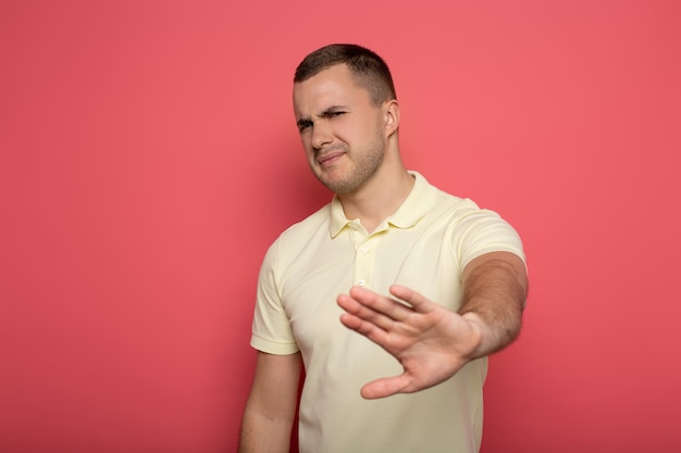 Displeased man showing stop gesture on pink