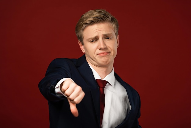 Displeased man showing thumb down on red background