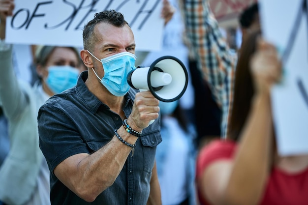 Displeased man wearing protective face mask while participating in a protest and shouting through megaphone